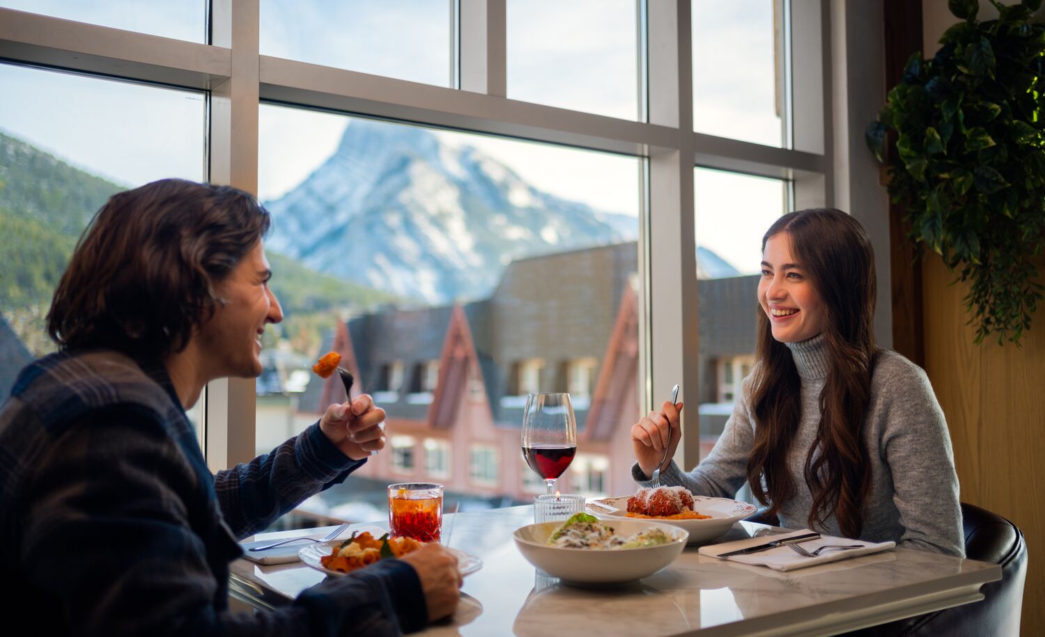 A couple dines at Lupo in Banff National Park with Mount Rundle out the window in the background.